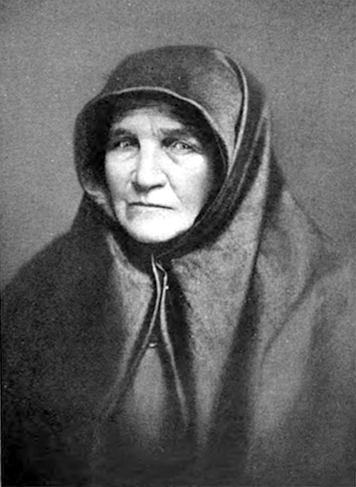 Crno-bela fotografija starije žene sa tamnim maramom preko glave i ramena, ozbiljnog pogleda.